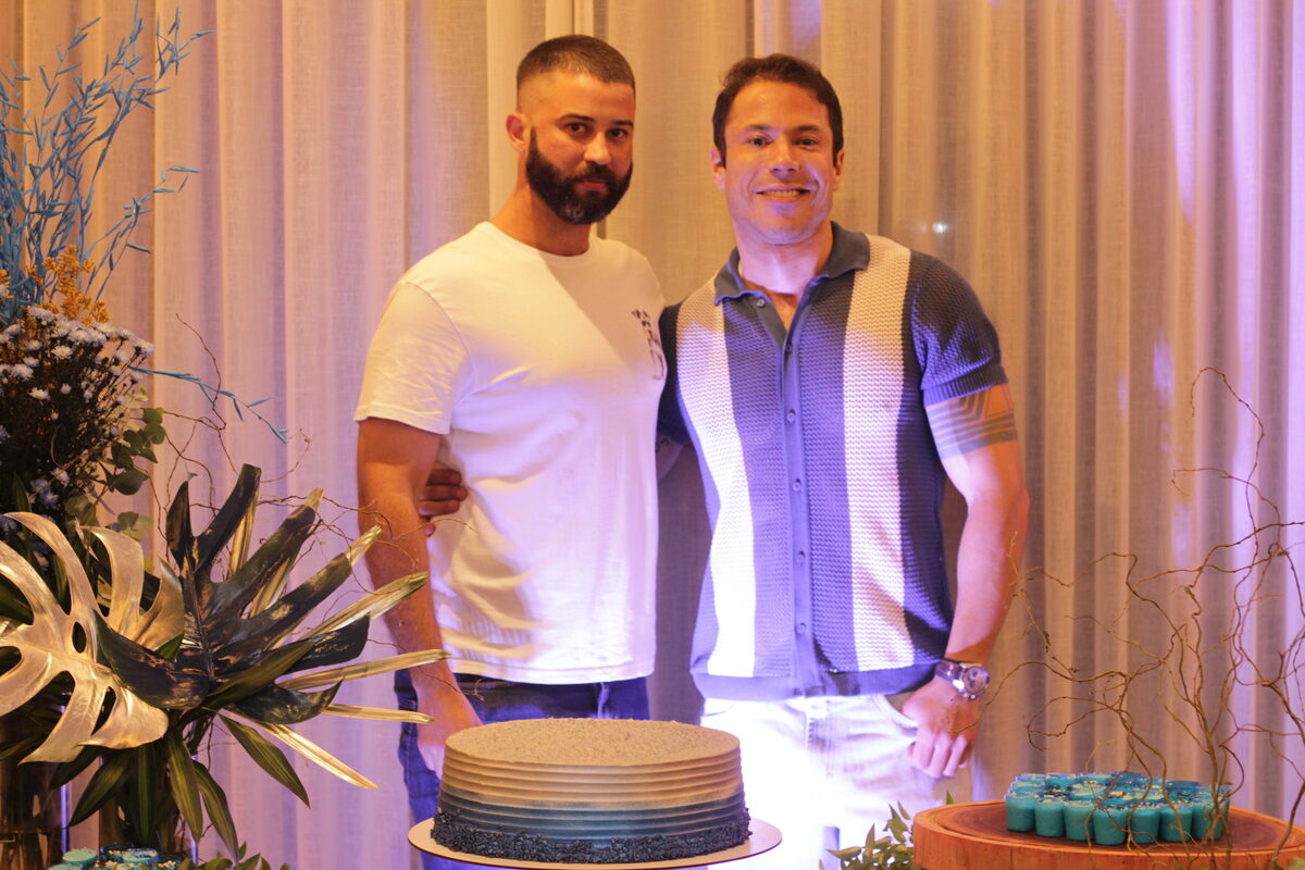 Dois convidados posando ao lado do bolo decorado com arranjos azuis e dourados