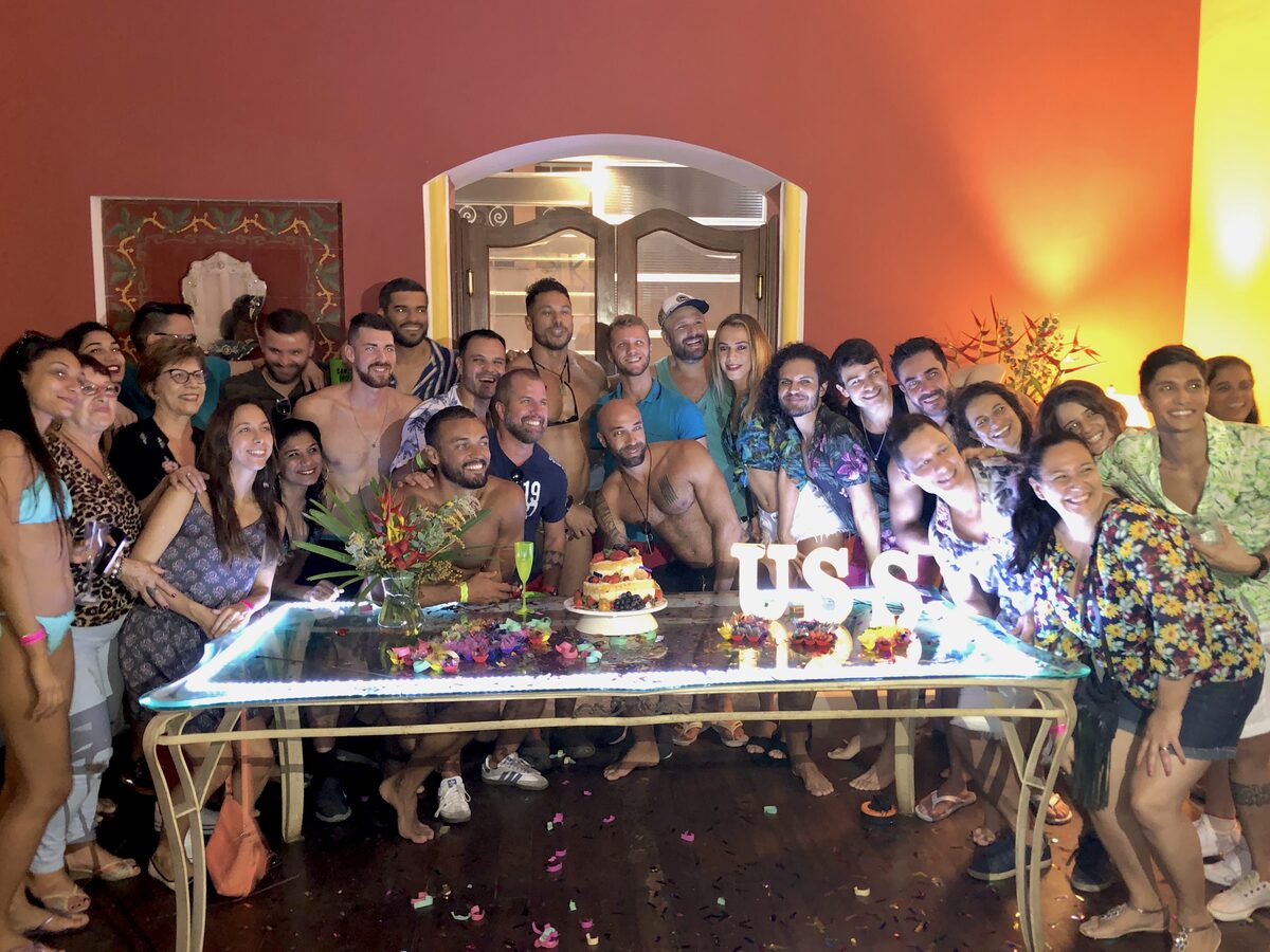 Grande grupo de convidados reunidos em torno da mesa de bolo iluminada
