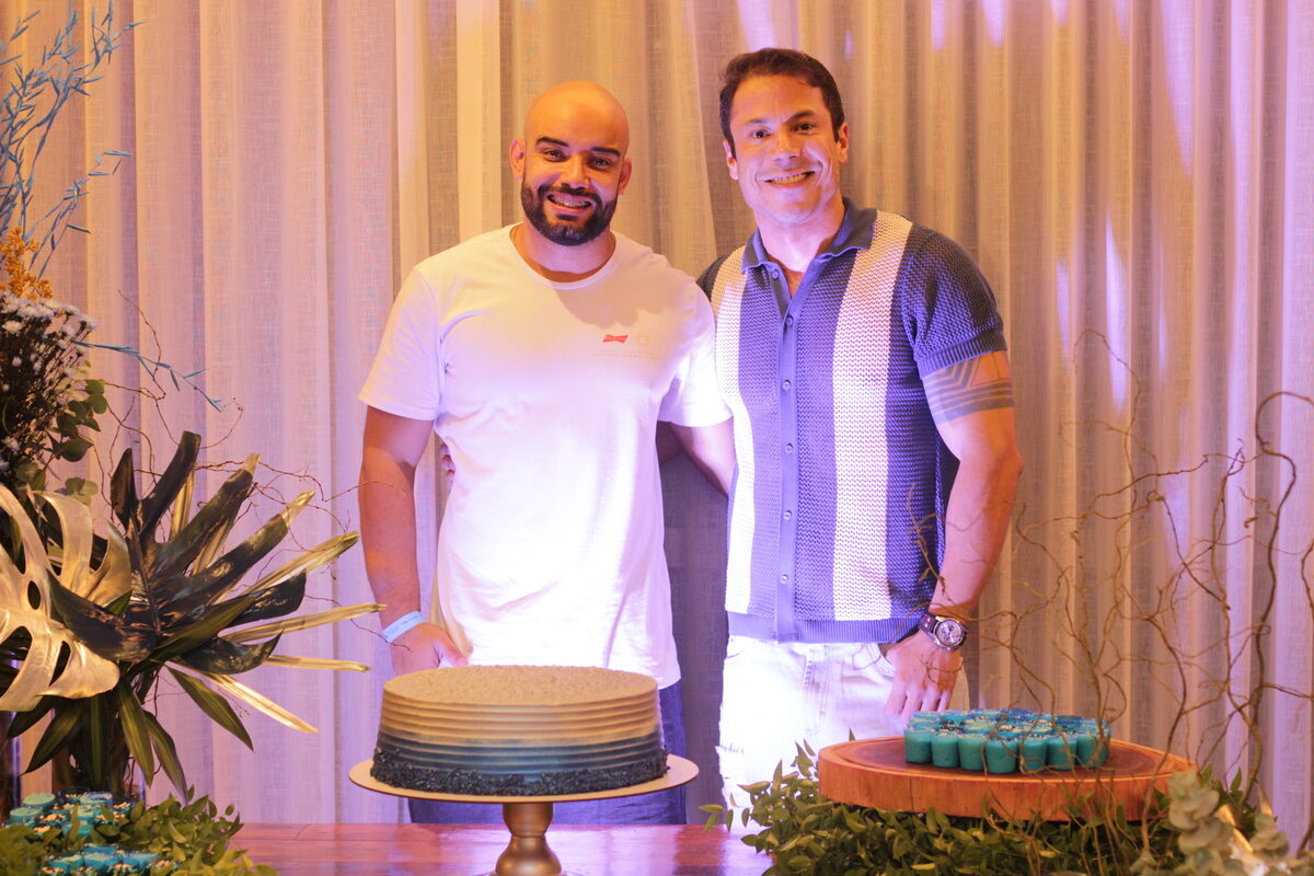 Dois homens posam ao lado de bolo degradê azul com decoração elegante - 7a Edição